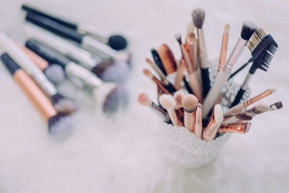 Pinsel und Make-up-Werkzeuge in einem Behälter auf einem eleganten Hintergrund.