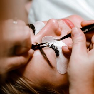 Eine Person erhält Wimpernverlängerung mit Baumwollpads und Pinzette.